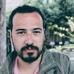 Portrait of a young man with facial hair, outdoors in a natural setting. Serious expression.
